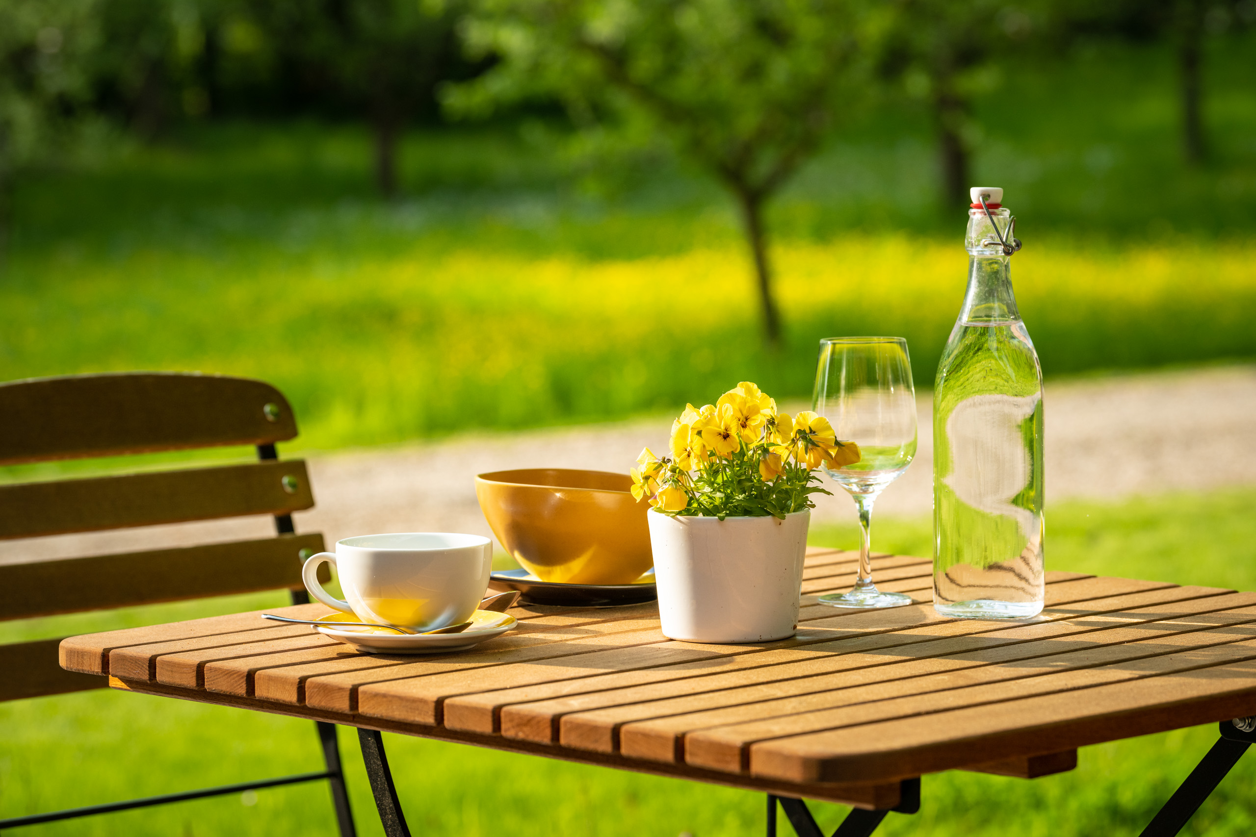 Outdoor table with coffee, yellow flowers, water bottle, and garden background