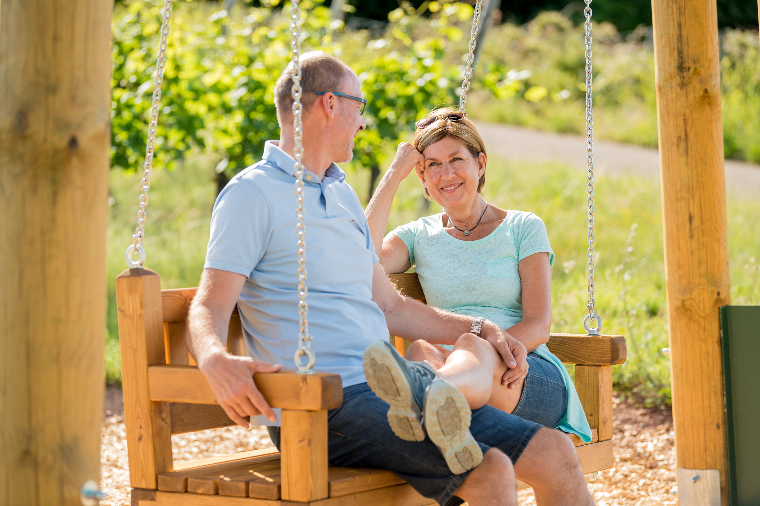 Mature couple sitting together on a wooden swing in a sunny garden