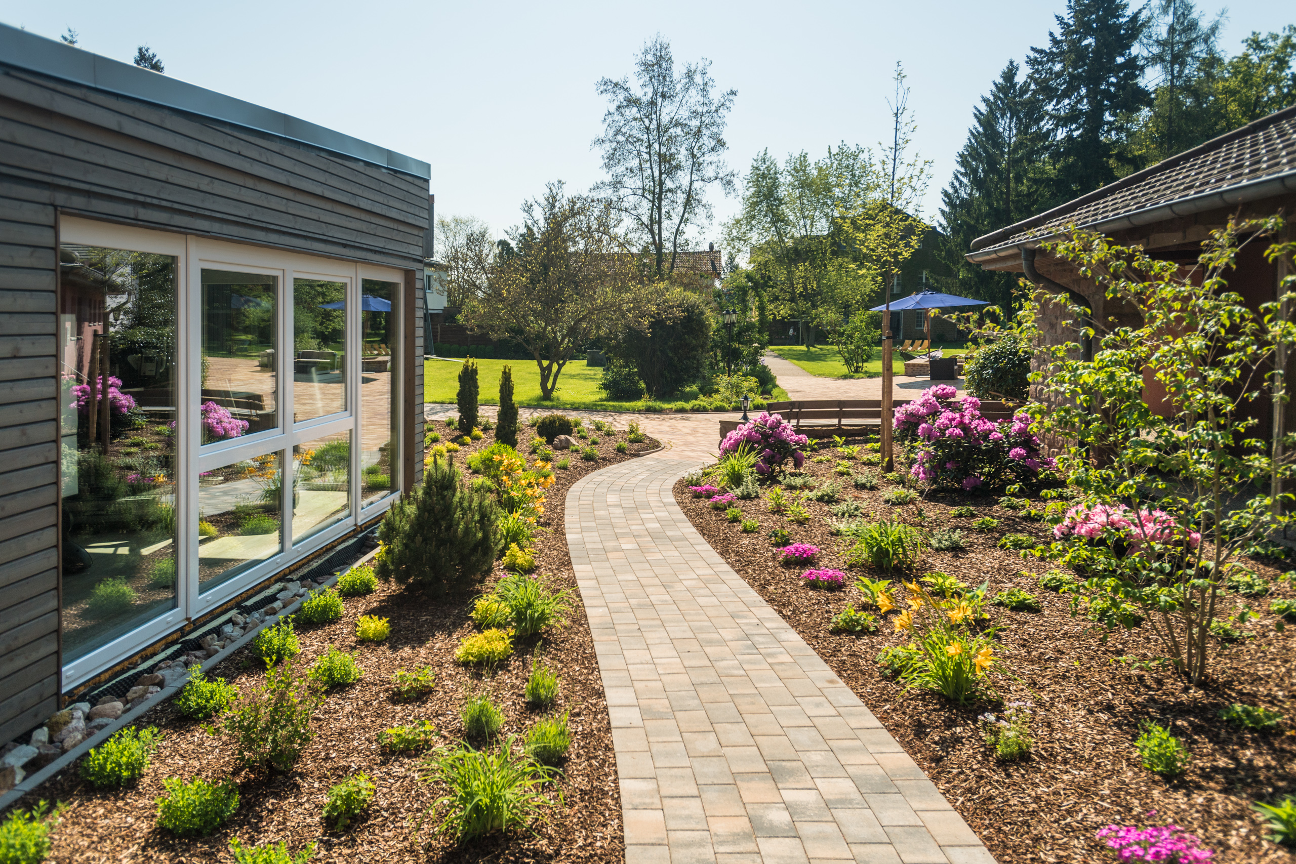 Curved stone path through landscaped garden with pink flowers and green plants