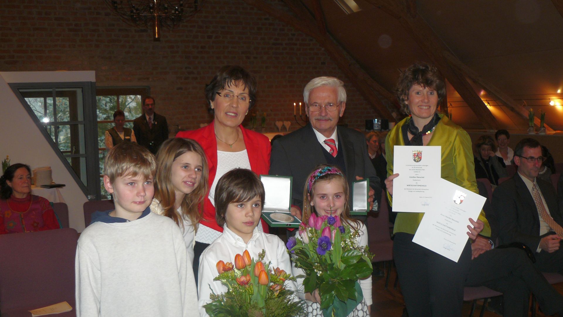 Gruppenaufnahme mit Blumen und Urkunden bei einer feierlichen Veranstaltung