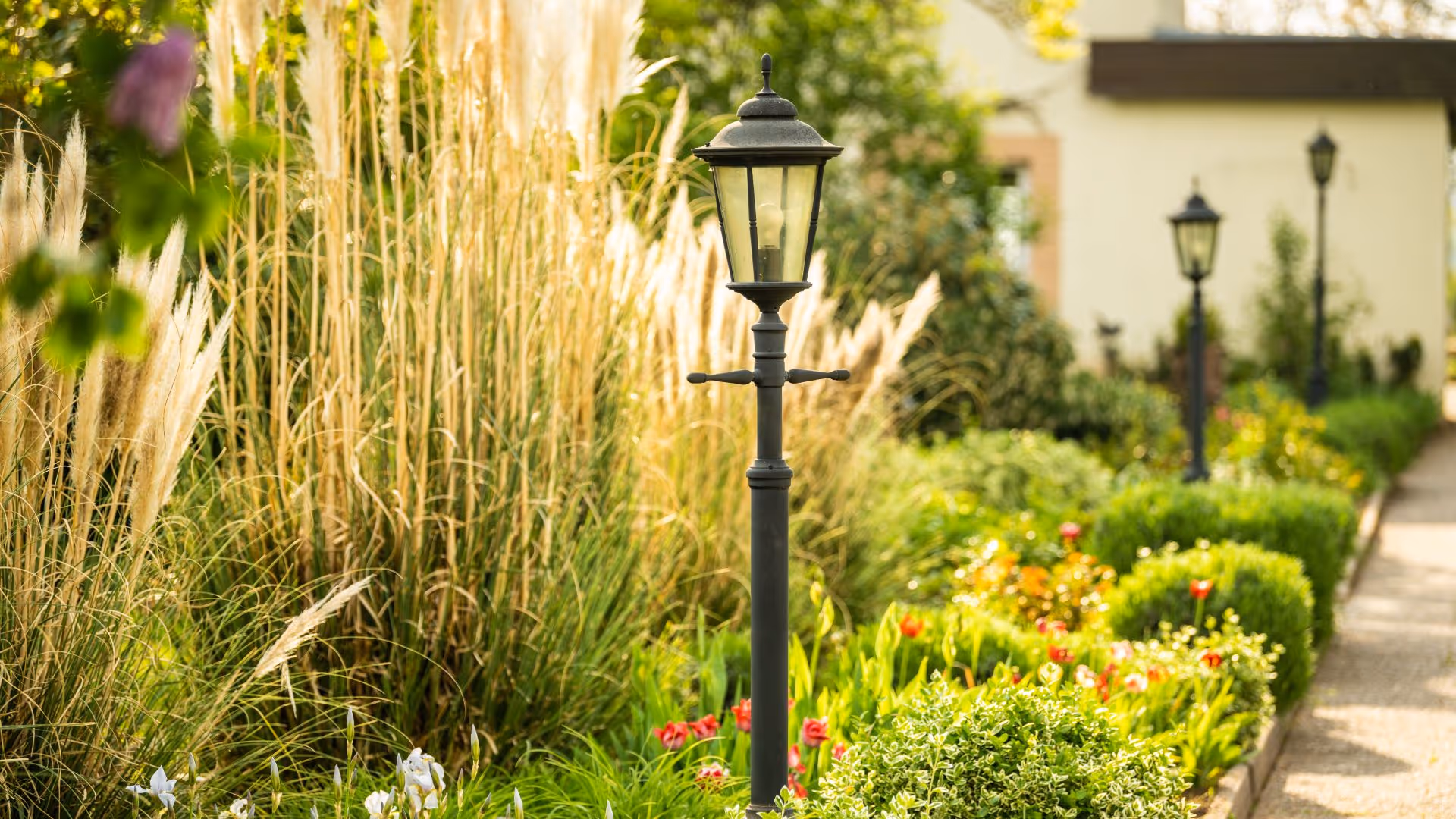 Ornate street lamp surrounded by lush garden with ornamental grasses and flowers
