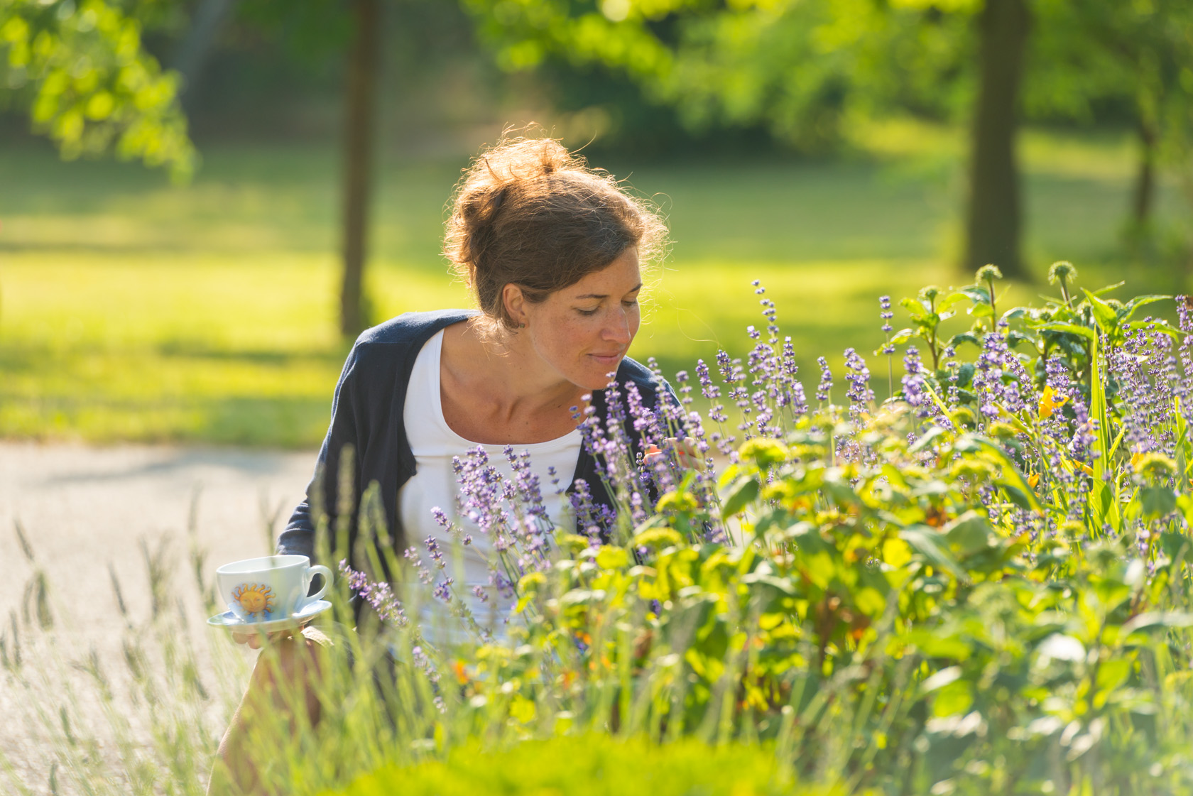 Woman enjoying tea among lavender flowers in sunny garden