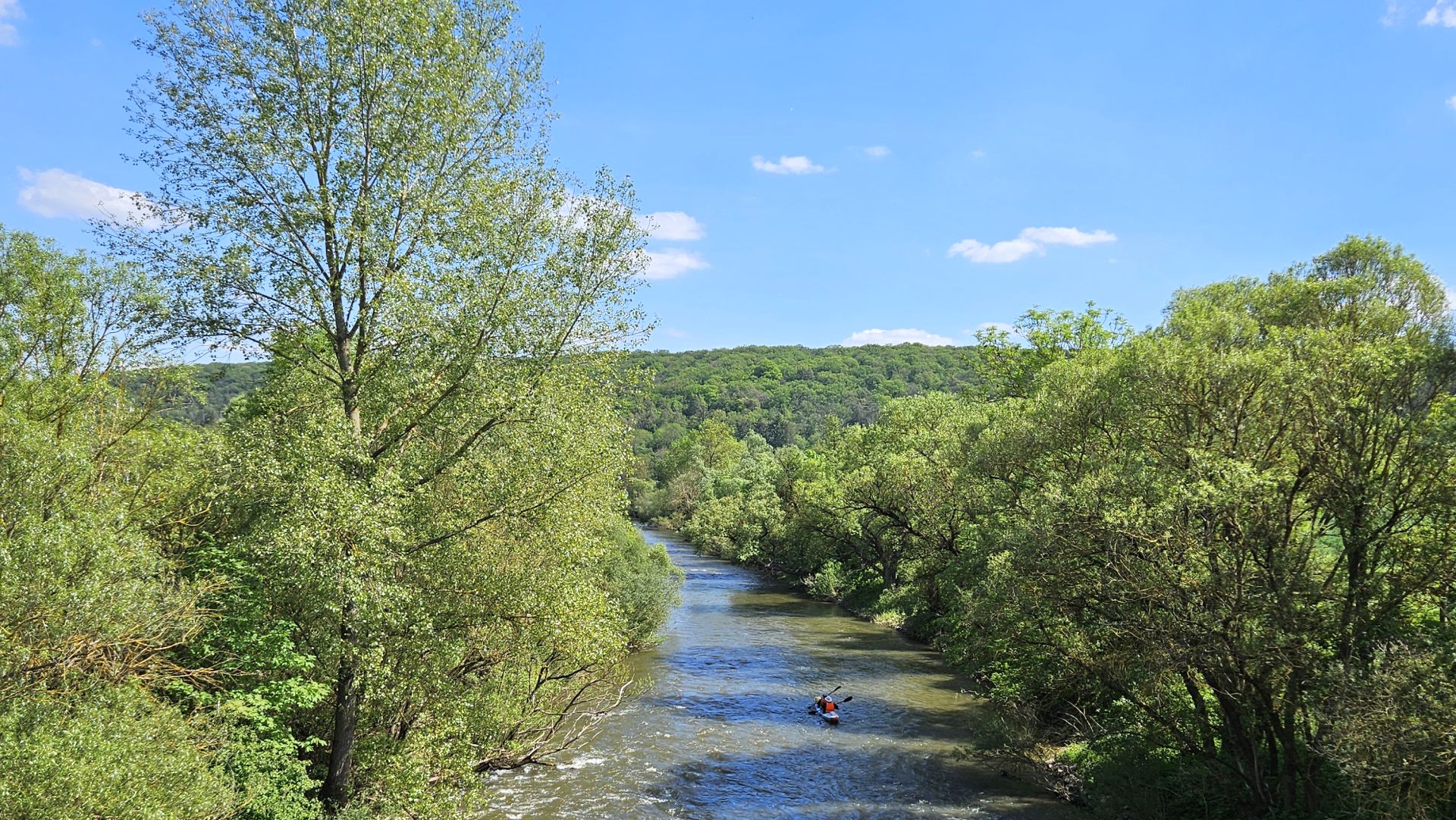 Kajak auf einem ruhigen Fluss, umgeben von grünen Bäumen und Hügeln