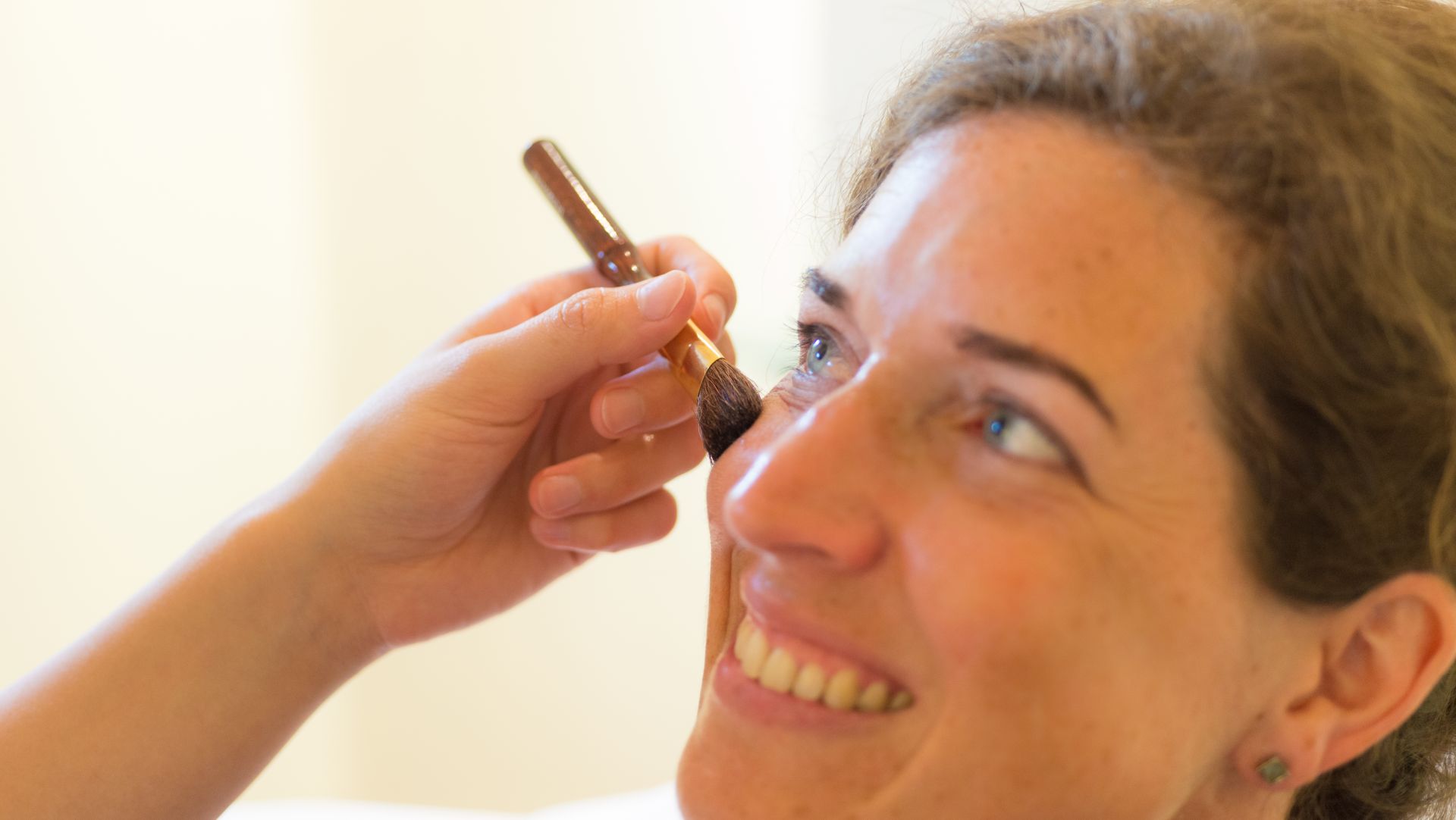 Smiling person applying makeup with a soft makeup brush