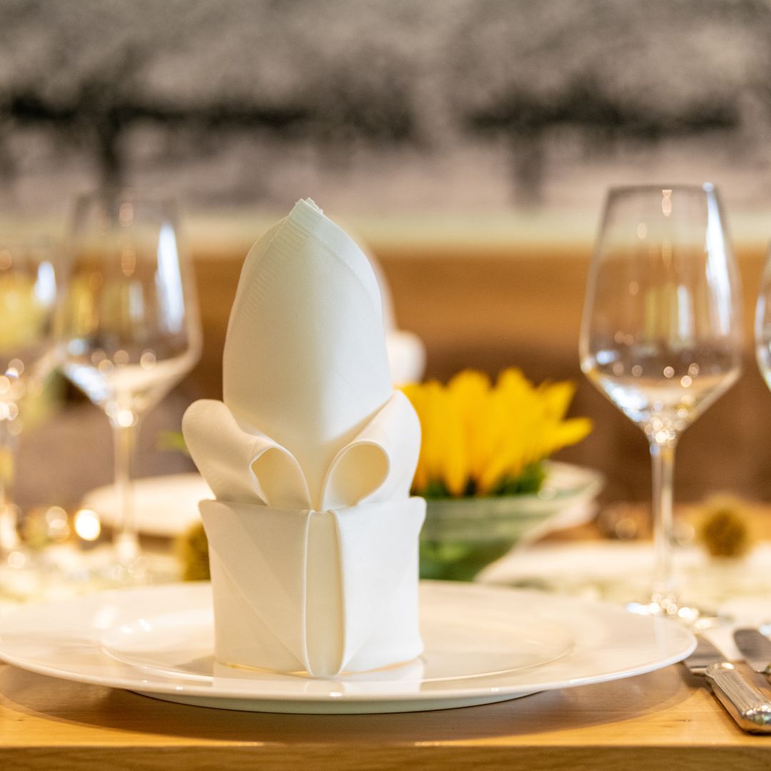 Elegantly folded white napkin on a table with wine glasses and sunflower