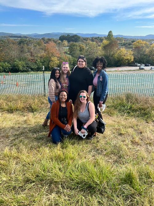 A joyful gathering of young adults supported by Kate's Club, posing on a grassy hill with a serene landscape behind them, embodying connection and support in the face of grief.
