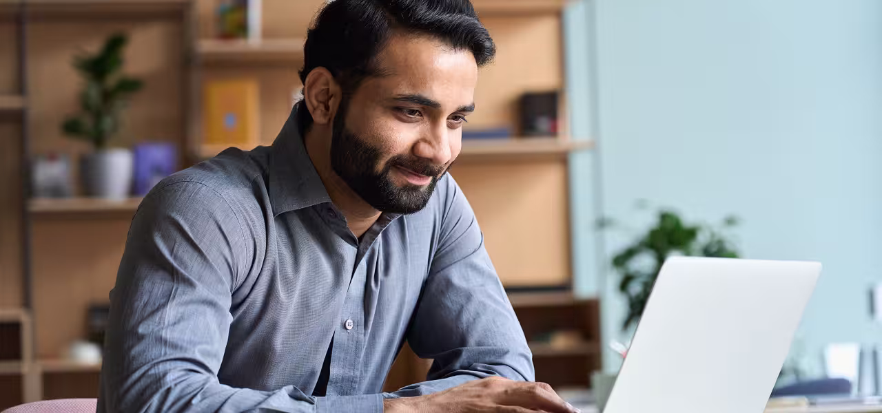 Hombre sonriente trabajando en su portátil en casa para ilustrar la historia del voto online de concepto a realidad