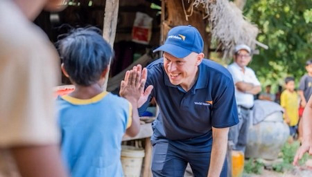 Tres personas sentadas alrededor de una mesa observan un monitor con un mapa mundial coloreado, en lo que parece ser una reunión de trabajo.