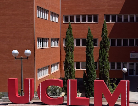 Edificio marrón grande con árboles delante y las siglas de la UCLM.