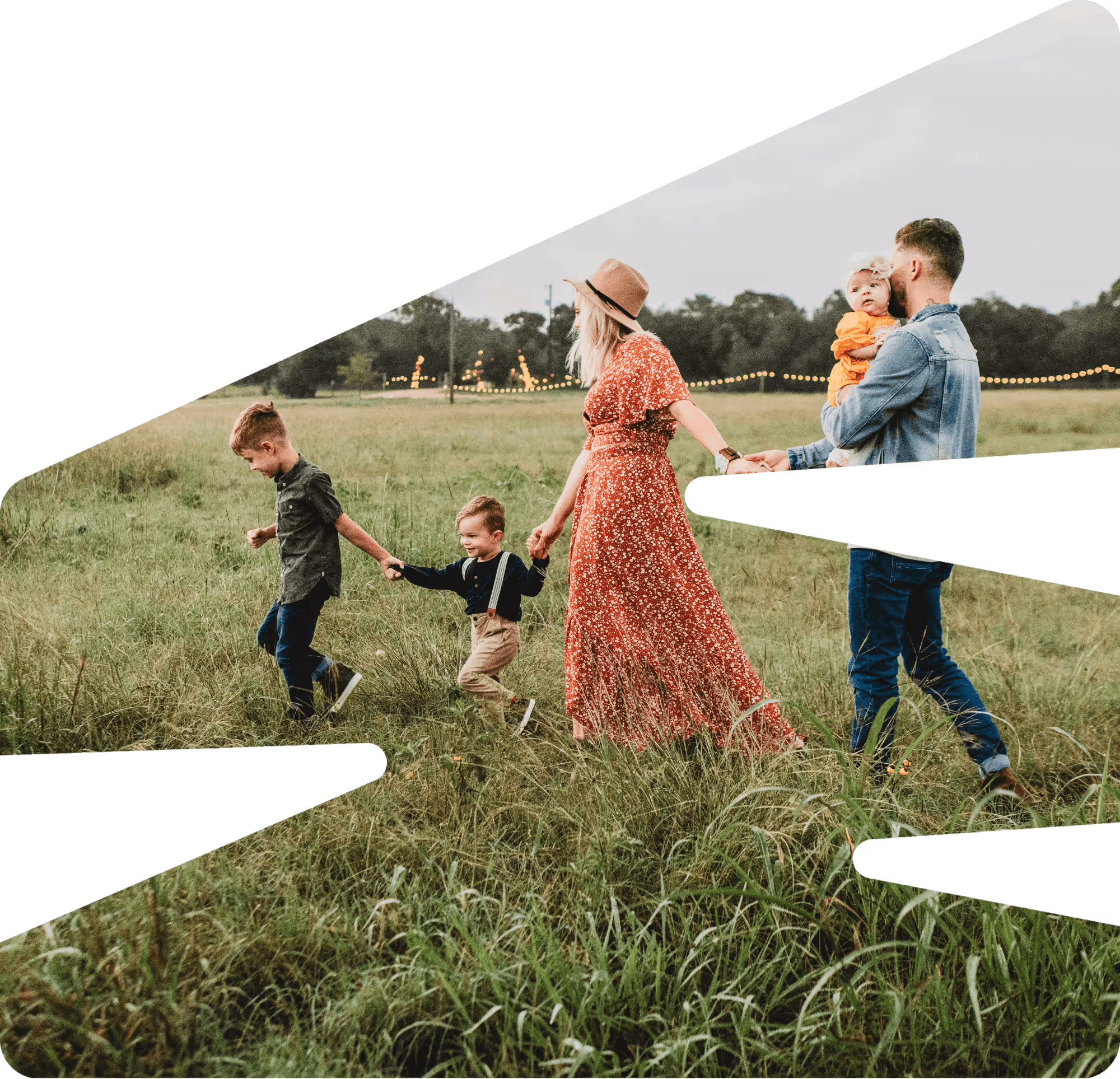 Family of four walking on a forest path covered with autumn leaves, with a child on the father's shoulders.
