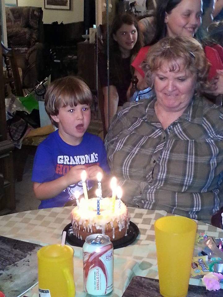 Young grandson and grandma sitting at the table with a cake with lit candles