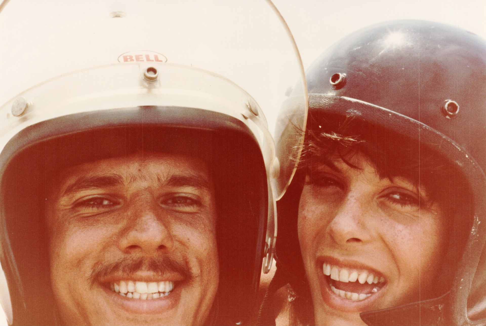 A man wearing a white motorcycle helmet is taking a picture with a woman in a black motorcycle helmet.
