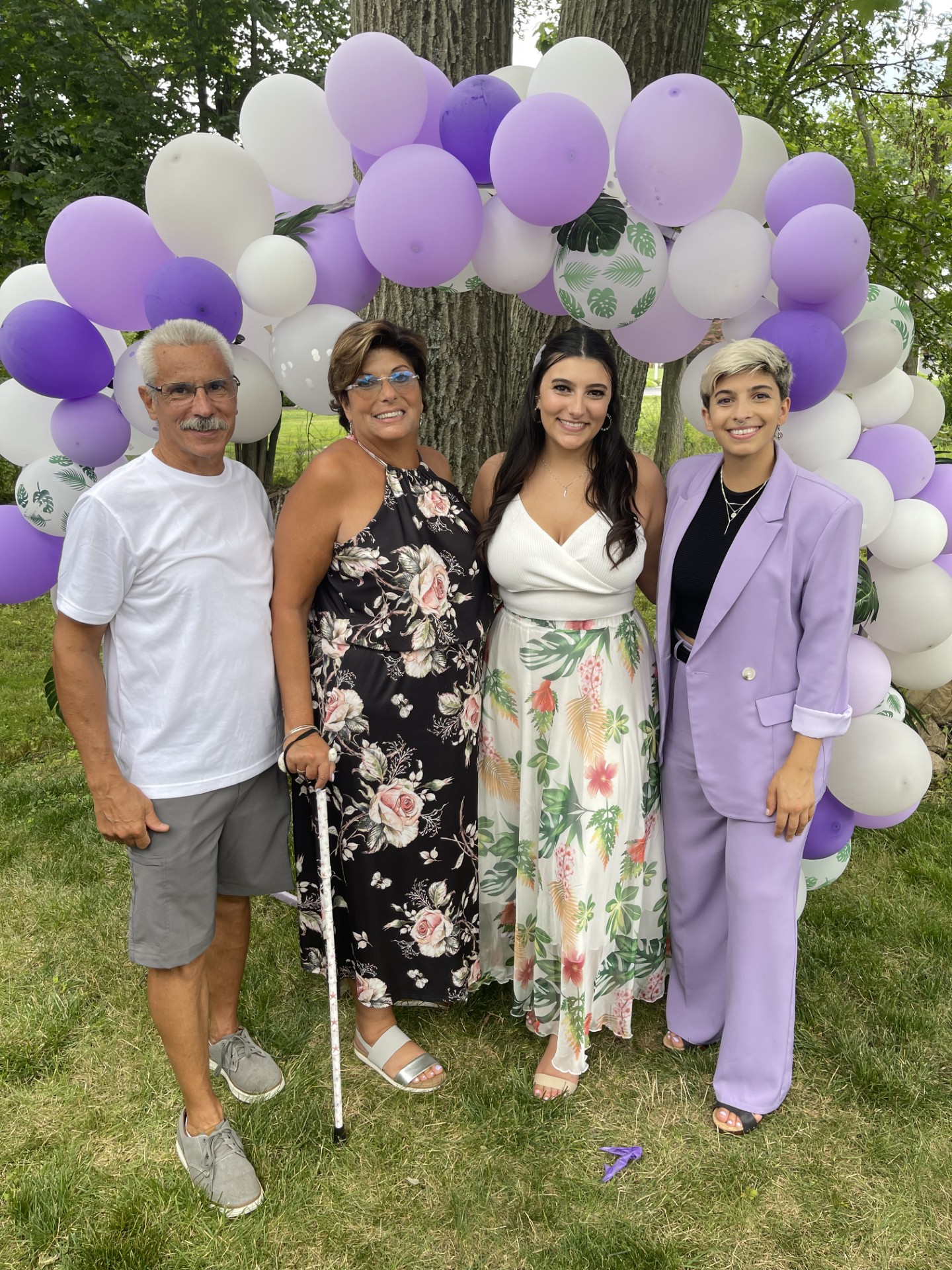 A group of 4 people standing in front of a balloon arch, smiling.