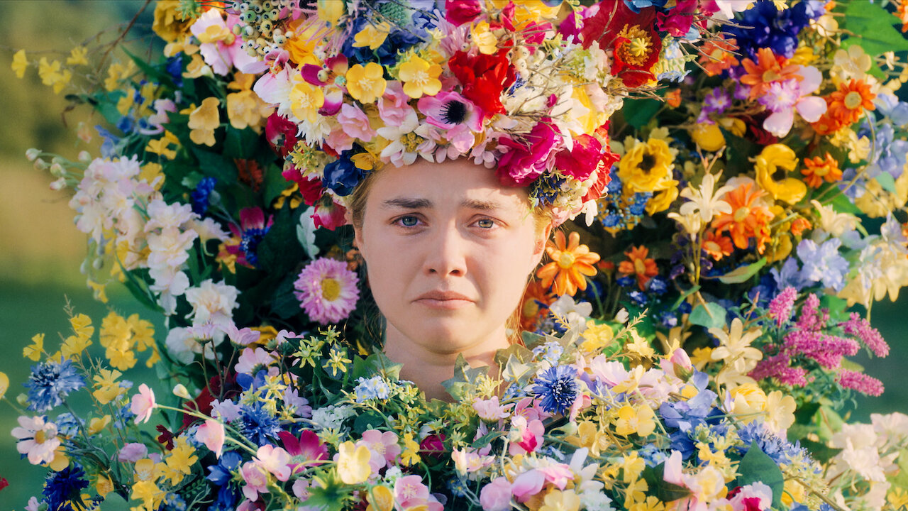 A woman frowns and cries while covered head to toe in colorful flowers.