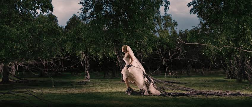 A woman in a wedding dress is running while getting stuck in the branches from trees.
