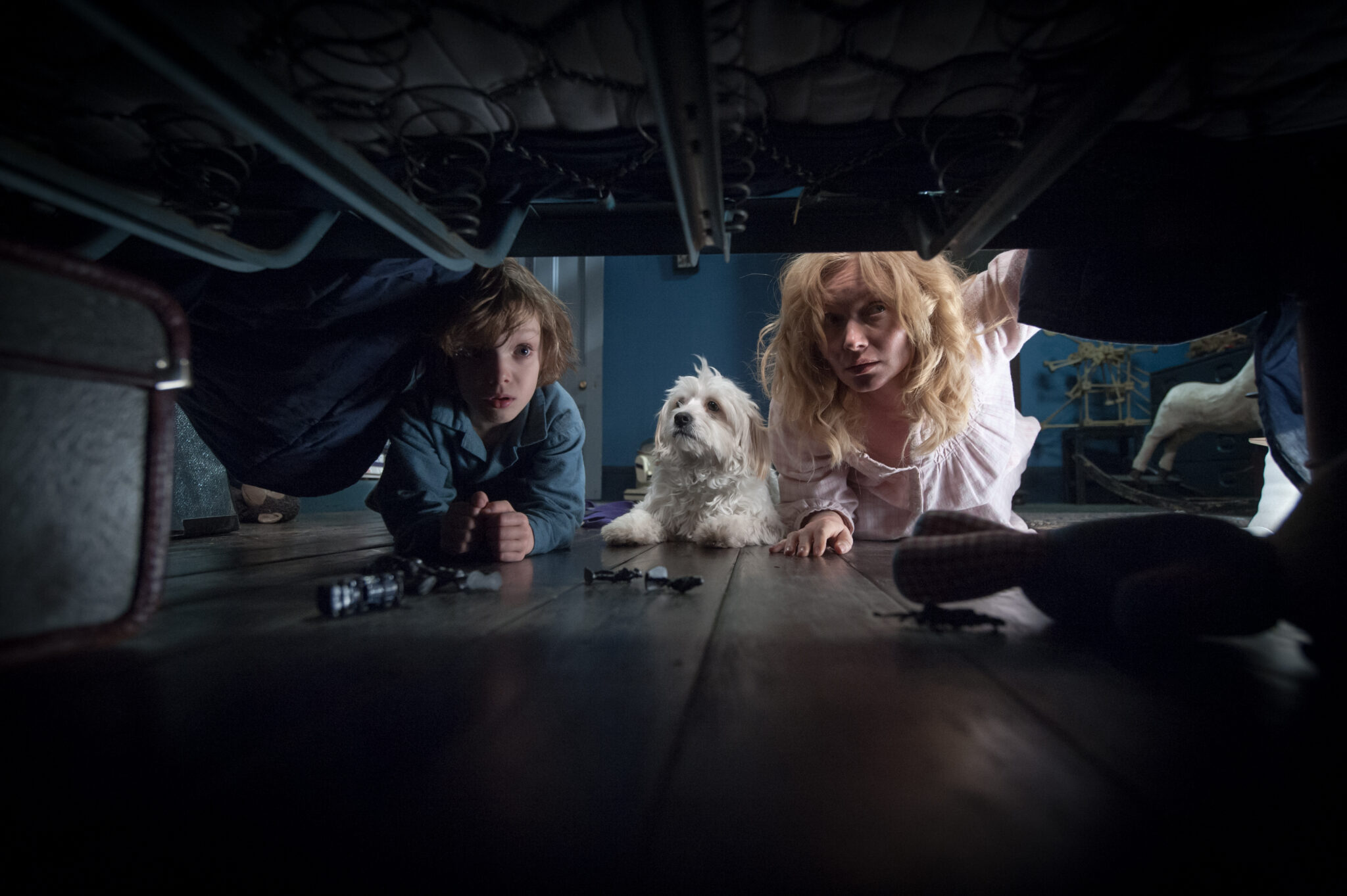 A mother, son, and dog all look under a bed to check for monsters.