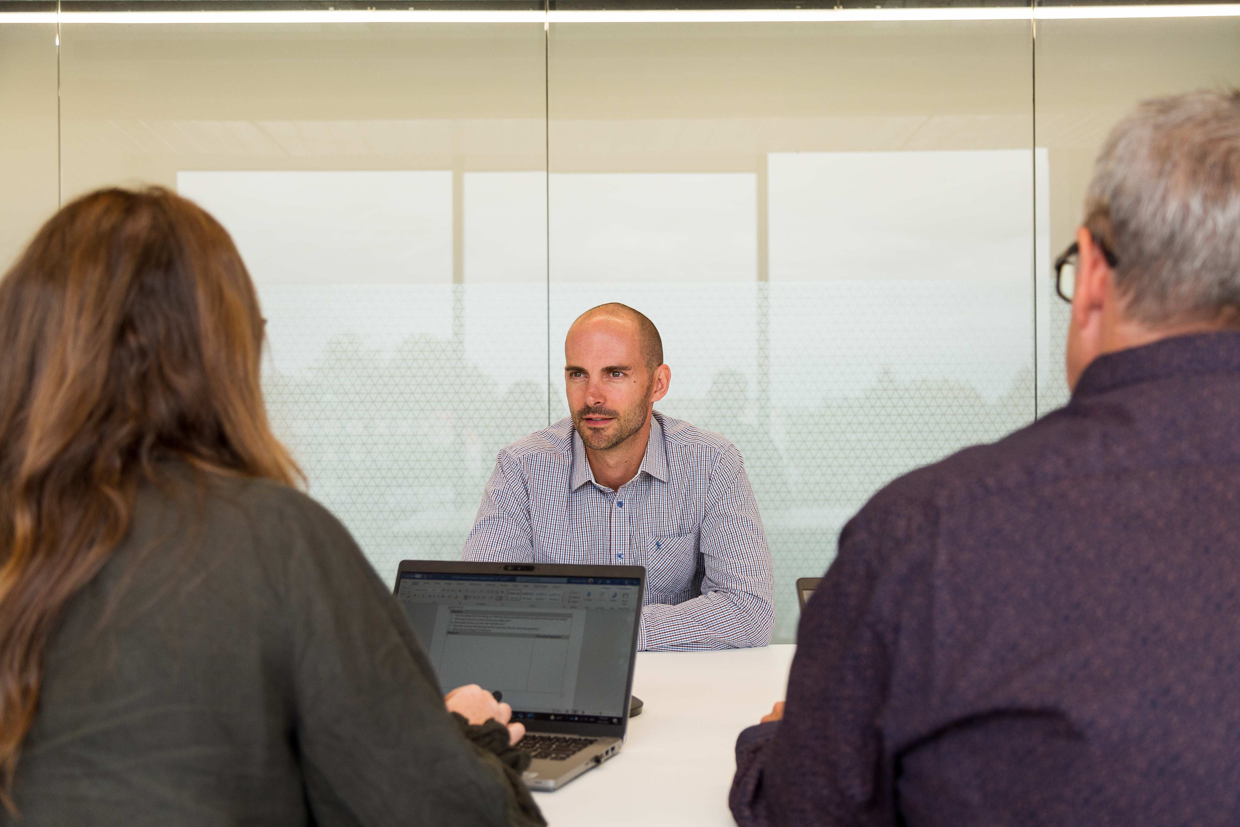 2 people in front of laptops interviewing a man