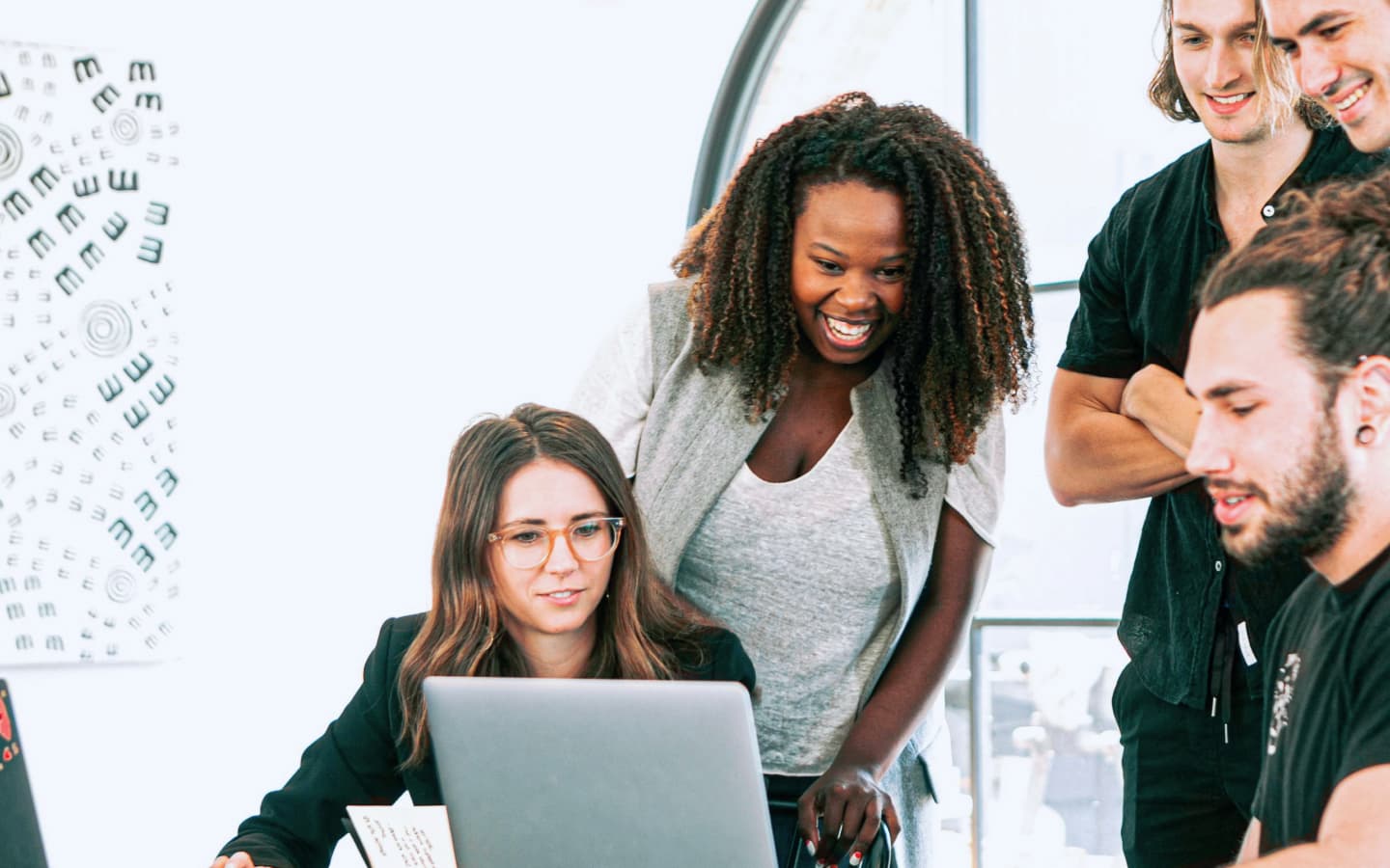 Groupe de cinq personnes échangeant autour d’un ordinateur dans un bureau moderne et lumineux.