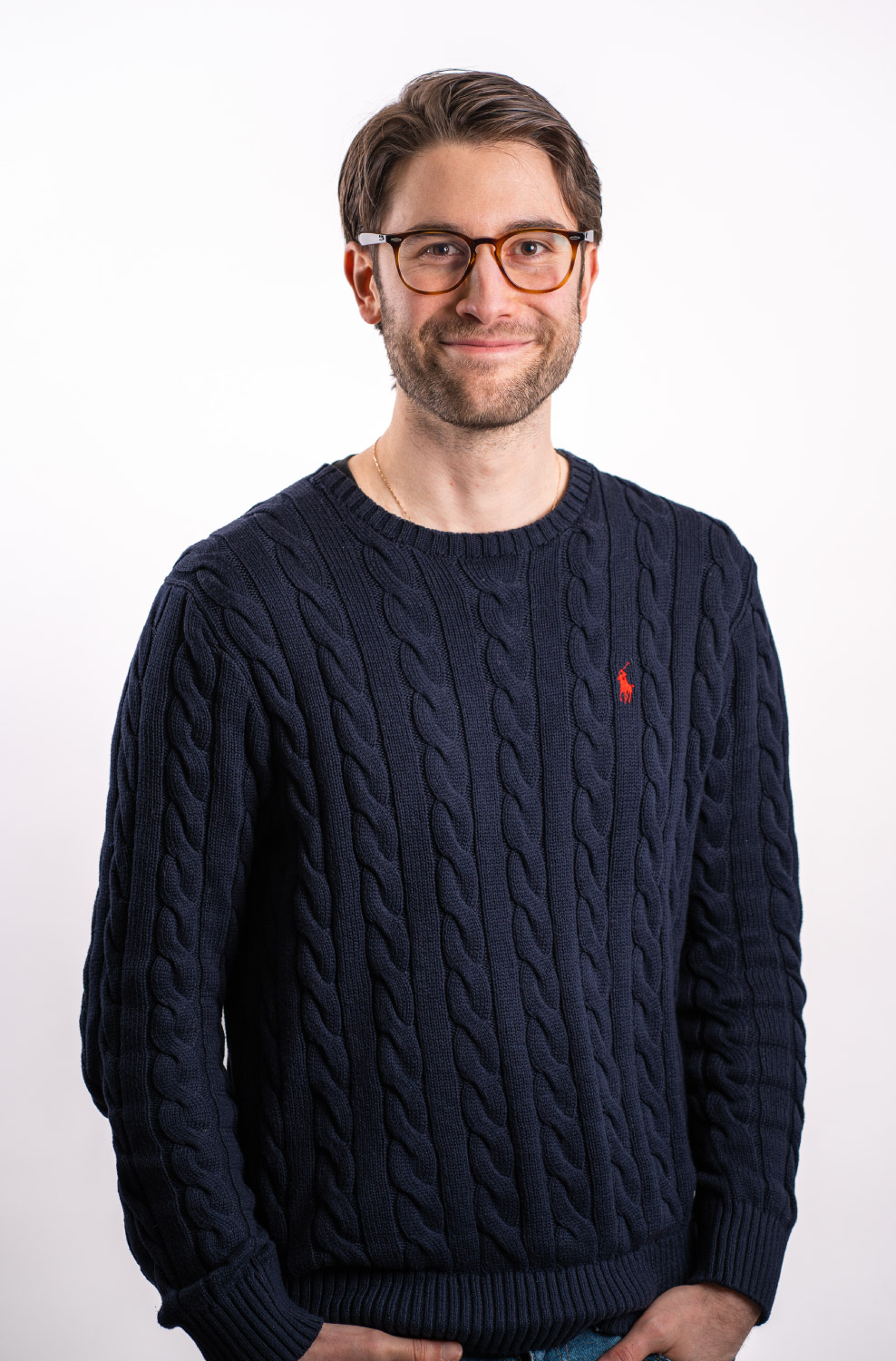 Ein Portrait von einem Mann mit einer Brille auf und einem dunkelblauen Ralph Lauren Pullover an.