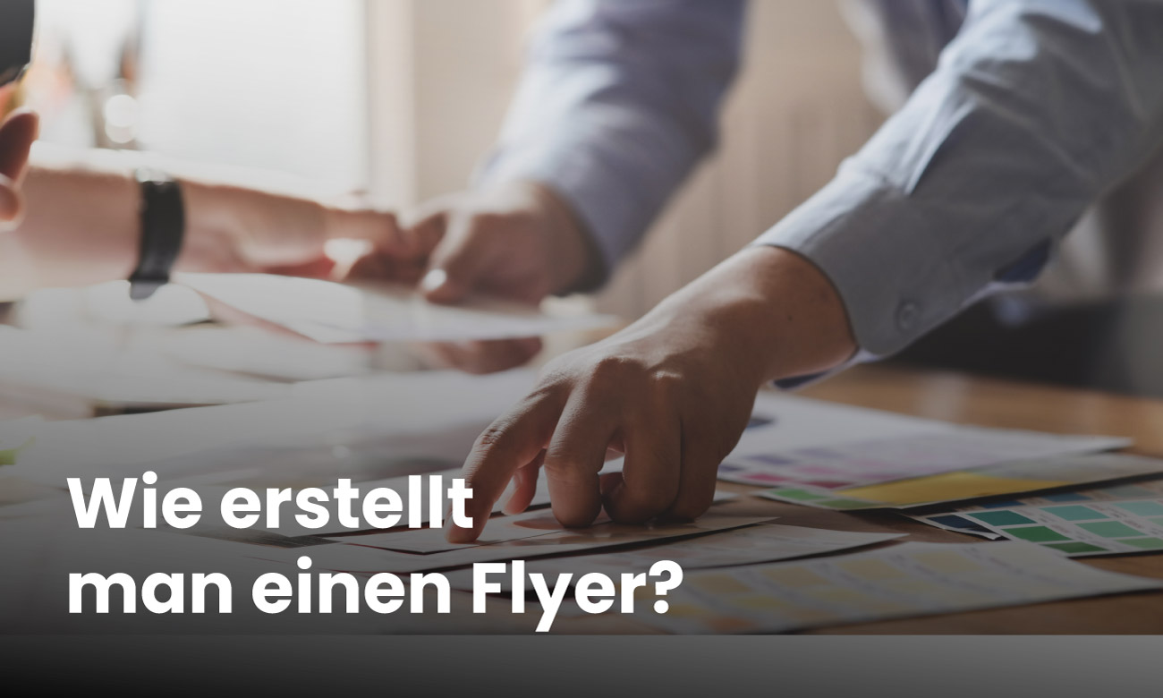 Hände von einem Mann die gerade einen Flyer anheben der auf einem Tisch mit vielen anderen Flyern liegt
