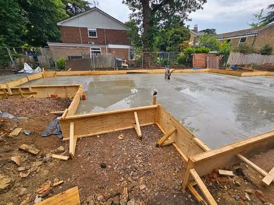 Freshly poured concrete foundation slab for a building with wooden framing and surrounding residential houses.