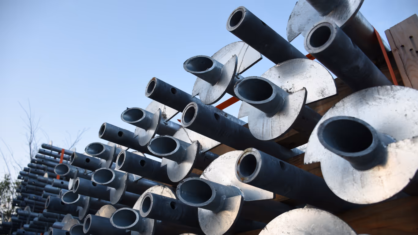 Stacked metal helical ground screws with wide flat circular plates under clear blue sky.