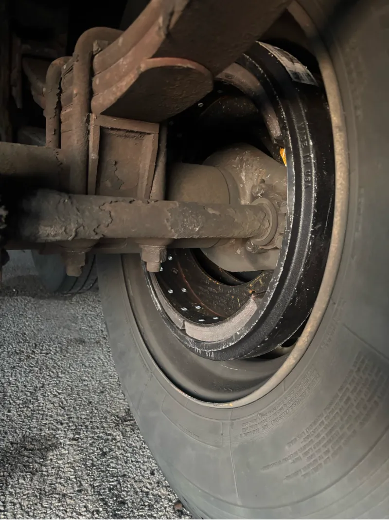 Brake drum inspection showing worn suspension components and dust buildup around the wheel assembly.