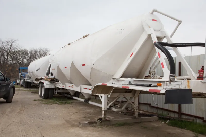 Heavy-duty bulk trailer service shows white pneumatic tanker parked outdoors with hoses attached and P406 marking visible.