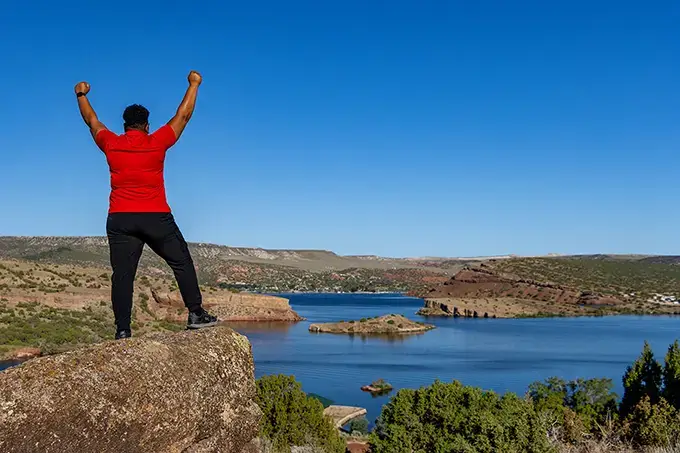 Work-Life Harmony & Burnout Coach Brandy Biglow thriving on top of a beautiful landscape after long journey to coaching