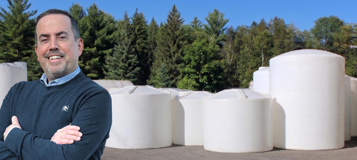 Percheron Plastic owner Matt Tanguay standing in front of white polyethylene storage tanks
