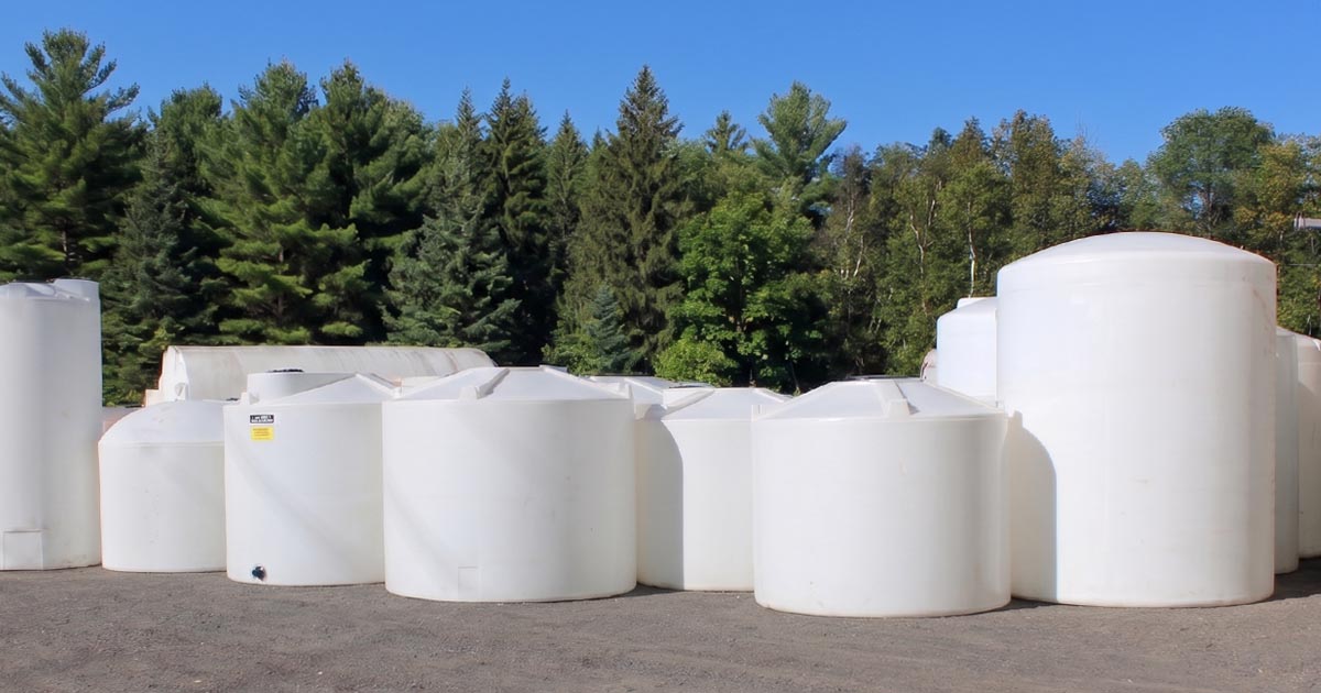 Rotomolded plastic vertical storage tank installed on a concrete pad at a farm, with agricultural equipment and Percheron Plastic branding visible