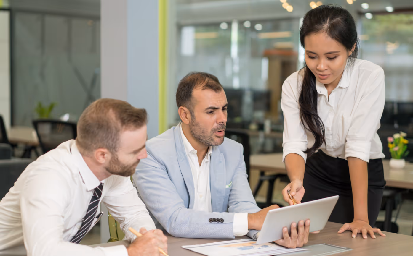 Three business professionals reviewing information on a tablet in a modern office.