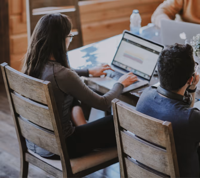 People working on laptops at a wooden table in a casual office setting.