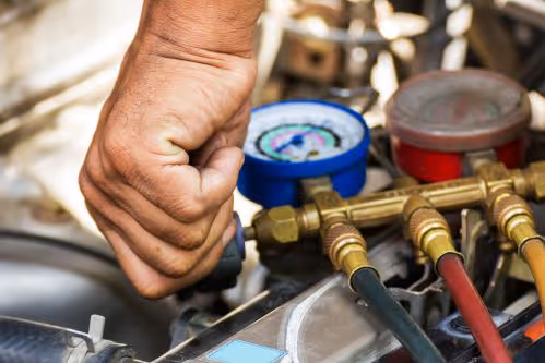 Hand adjusting valves on HVAC manifold gauges with various colored hoses connected.