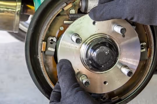 Gloved hands installing or inspecting a vehicle wheel bearing and brake drum assembly.