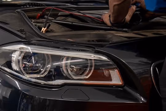 Close-up of a black car's headlight with a person working under the open hood.