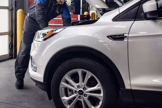 Mechanic inspecting the engine of a white Ford SUV inside a garage.