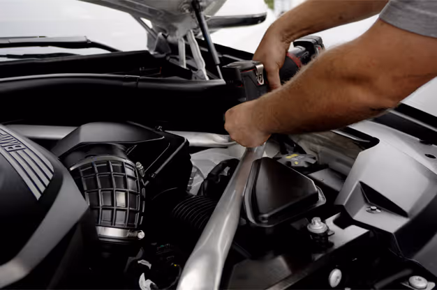Mechanic using a power tool to work on the engine of a car with the hood open.