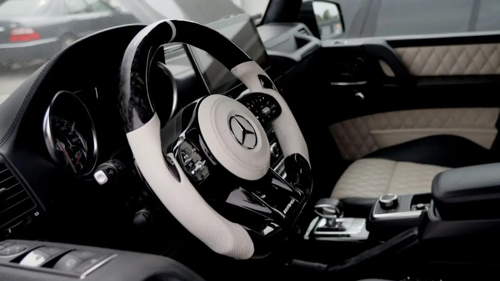 Interior of a luxury car featuring a white and black Mercedes-Benz AMG steering wheel and quilted leather seats.