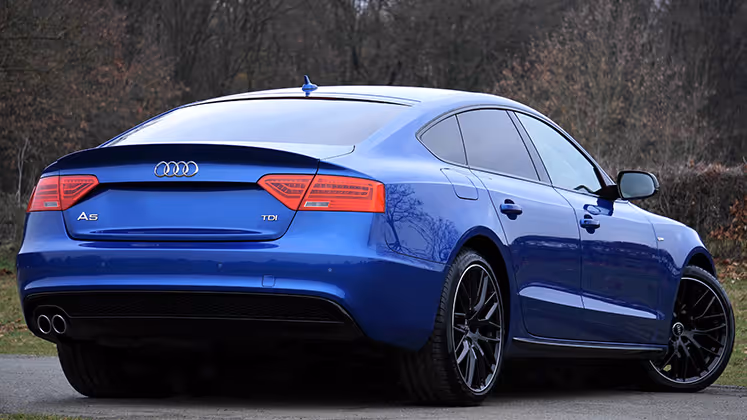 Blue Audi A5 TDI parked on a road with a forest background, showing the rear and side view.