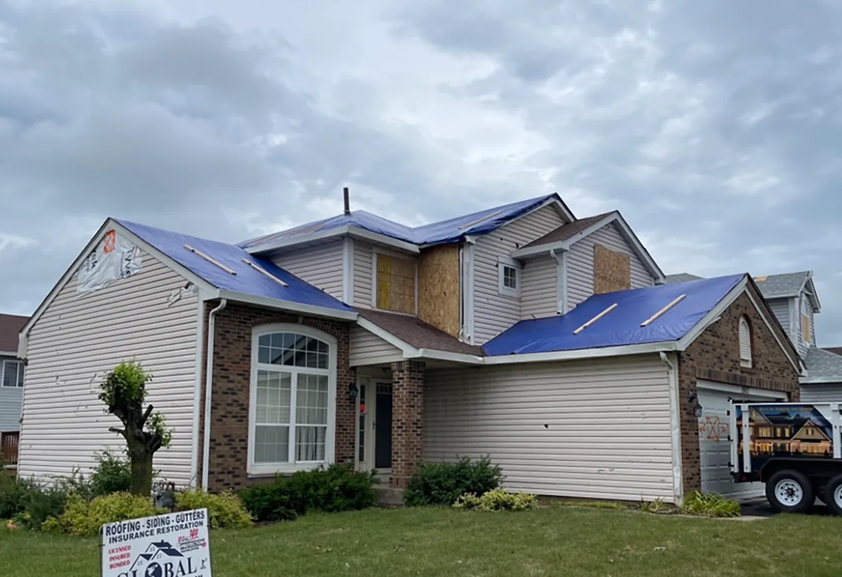 before photo of storm damage home with emergency tarp on roof.