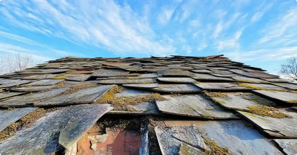 View of dark gray black slate roof with missing shingles, and a sunny blue sky