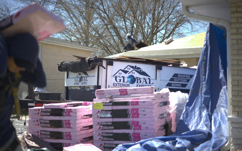 Global Exterior Experts trailer parked infront of residential roof project while roofer carrys shingle bundle on his back 
