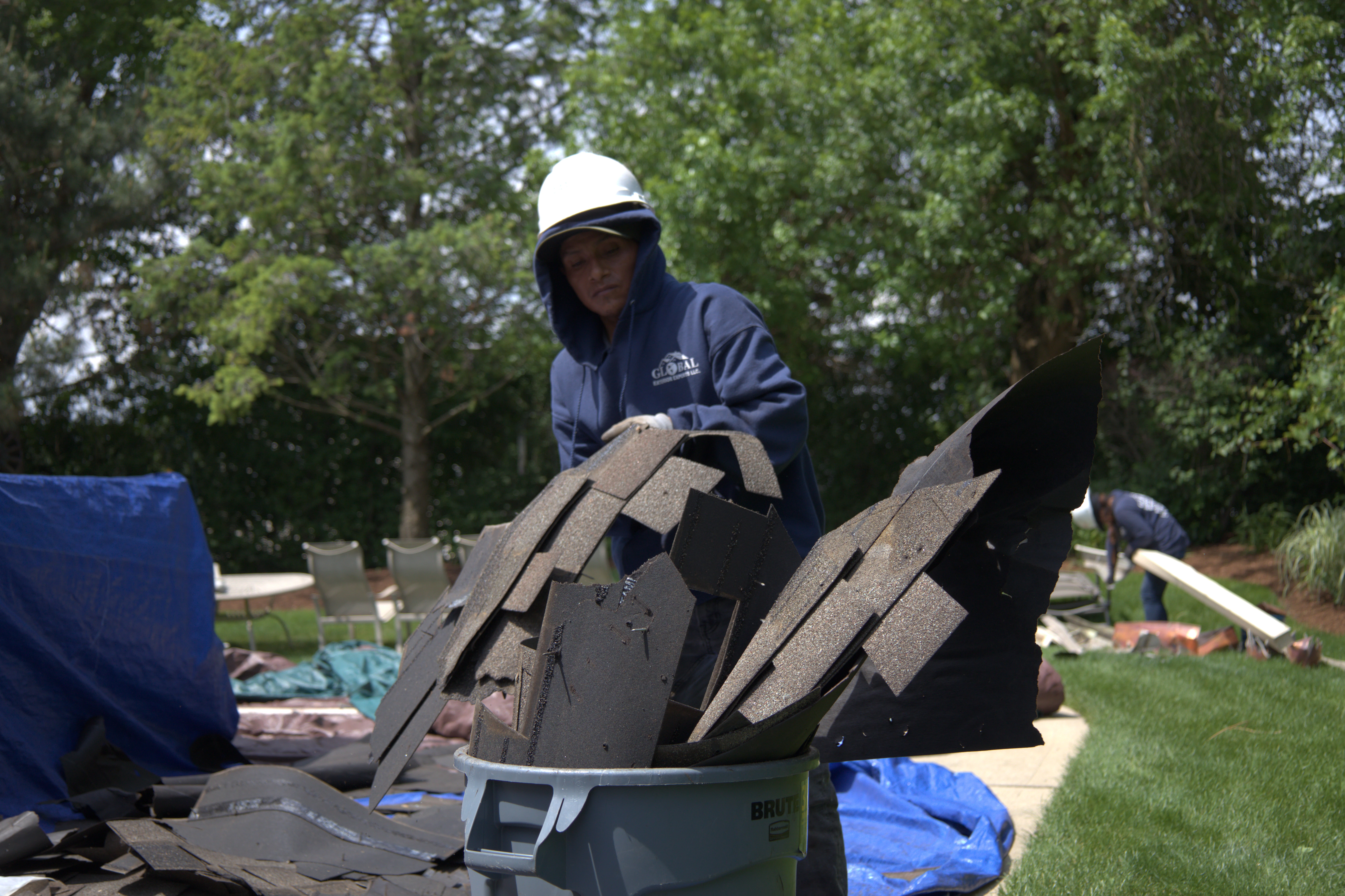 Roofer Throwing Away Shingles Into Garbage Bin After Roof Replacement