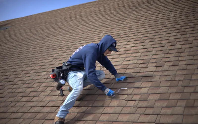Roofer Inspecting Hail Damaged Roof With Caulk