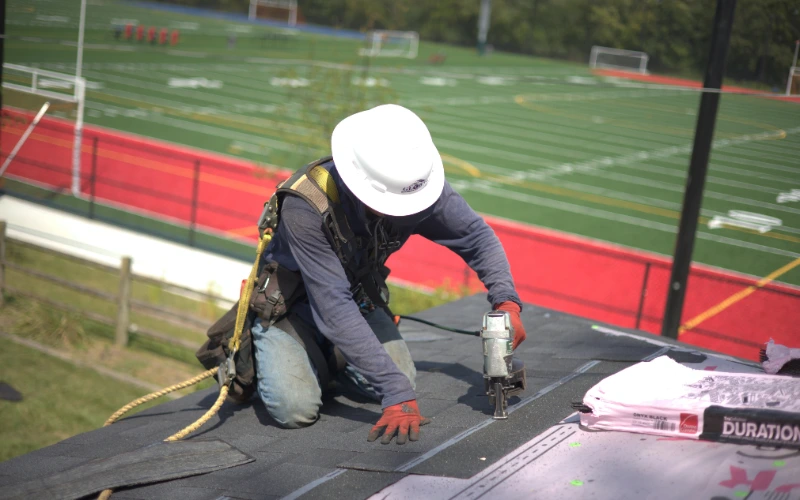 Installing Shingle Roof On Residential Home Infront Of Football Field