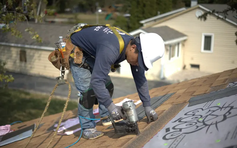 Roofer putting on shingles on residential property home.