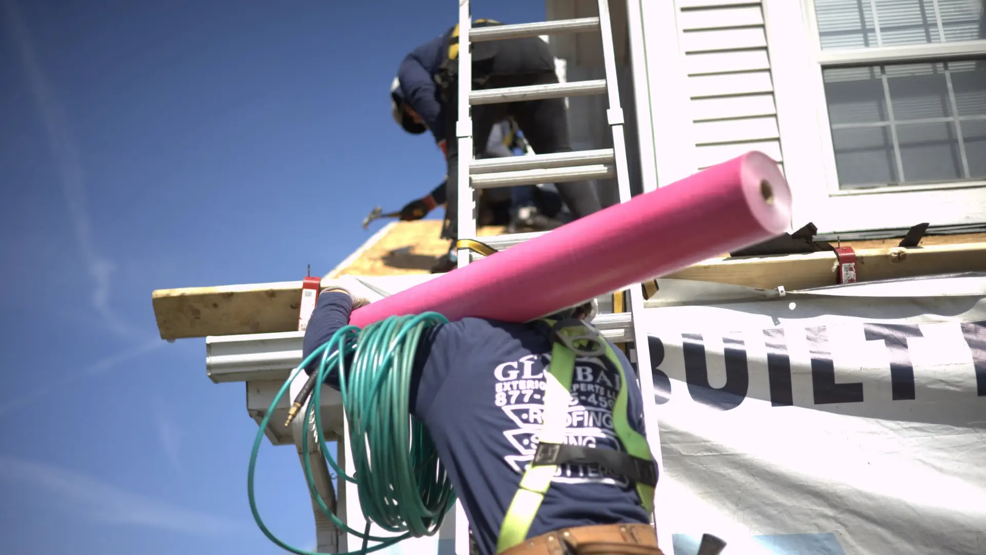 Professional roofer carrying pink underlayment up a ladder to the roof