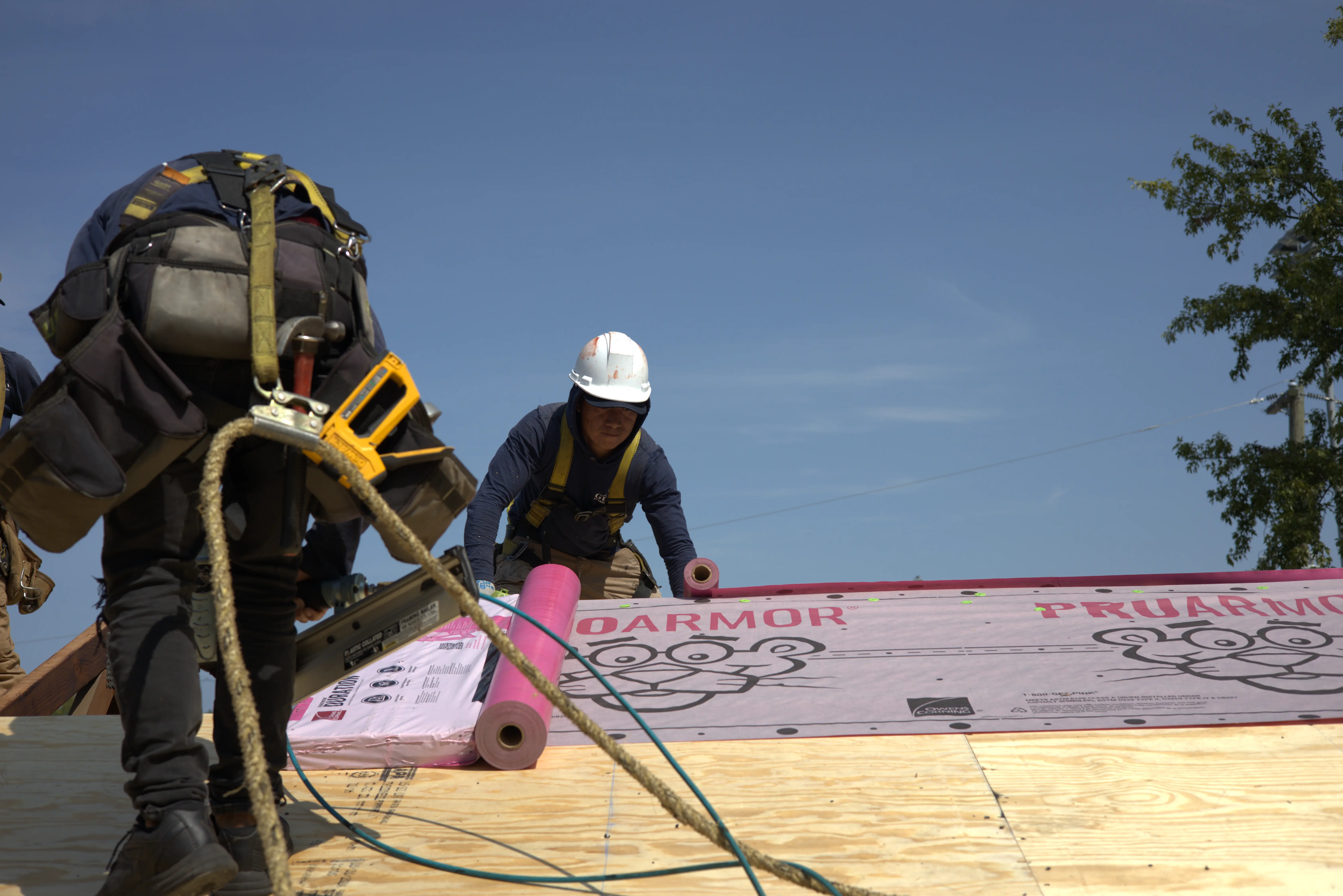 Two professional roofers on the roof installing underlayment and a roof.