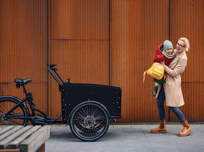 Mother carrying a young child towards a cargo bike 